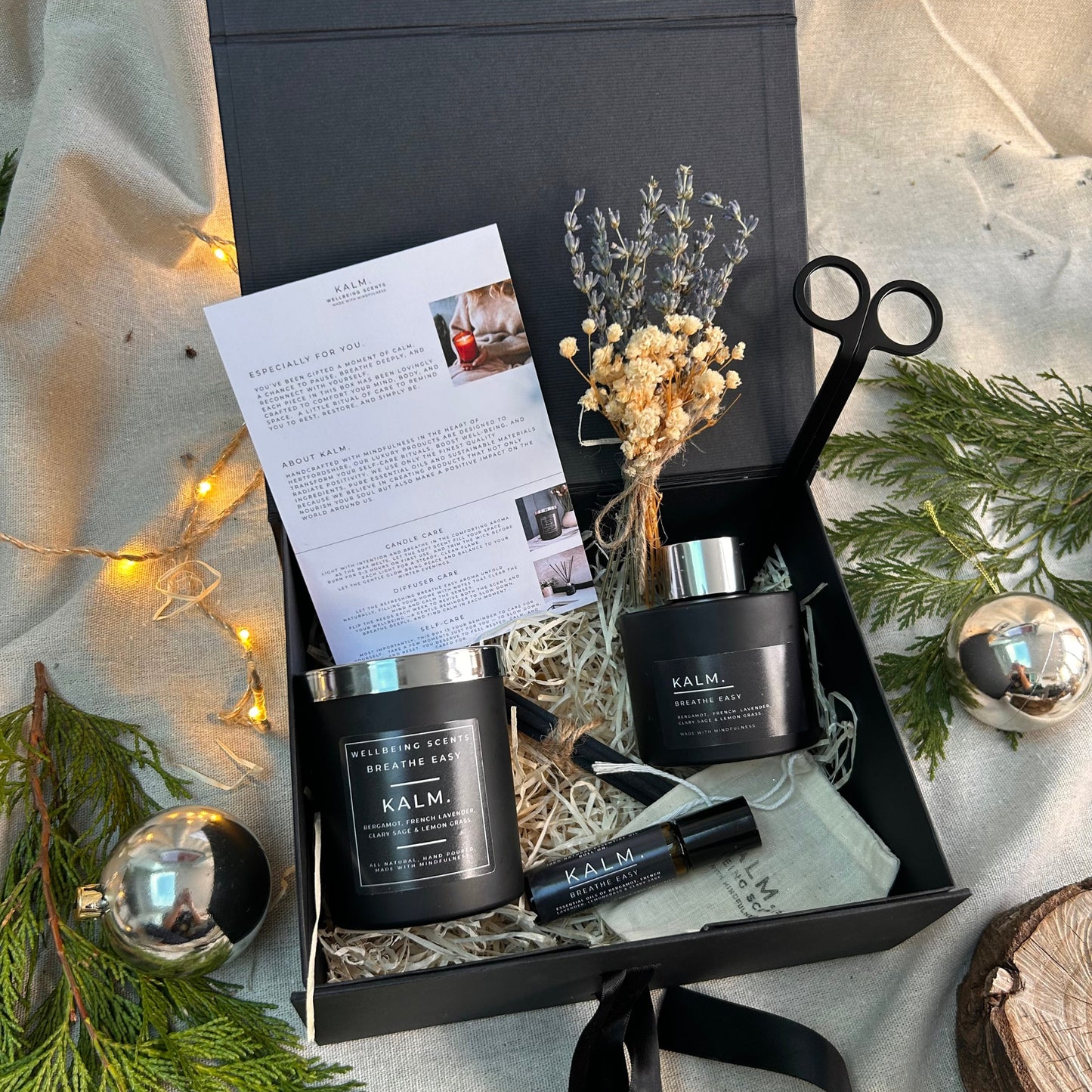Gift set with 'KALM' products including candles and a bottle, surrounded by decorative elements on a light background.